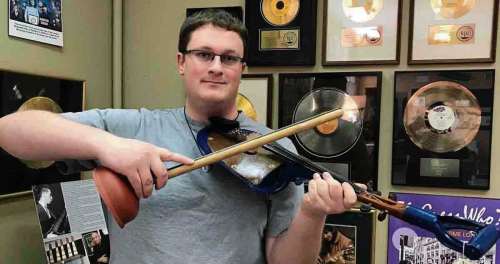 Photo by Bob Holliday 
Jared Warkentin poses at the St. Vital Museum with a “shovel fiddle” (and a plunger bow) once owned by Jimmy Moore.