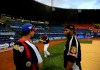 FILE - In this Nov. 27, 2013, photo, Anthony DeFrancesco, center, son of Tiburones head coach Tony DeFrancesco, left, practices his baseball swing as his father speaks with a player prior to a baseball game against rival Leones, at Estadio Universitario in Caracas, Venezuela. Major League Baseball is banning players from participating in the Venezuelan Winter League in one of the first public repercussions of new U.S. economic sanctions against the Venezuelan government. MLB said Thursday, Aug. 22, 2019, it is in contact with the U.S. government to determine how to proceed under the new sanctions against President Nicolás Maduro's administration and at least temporarily suspending involvement in the league. (AP Photo/Fernando Llano, File)