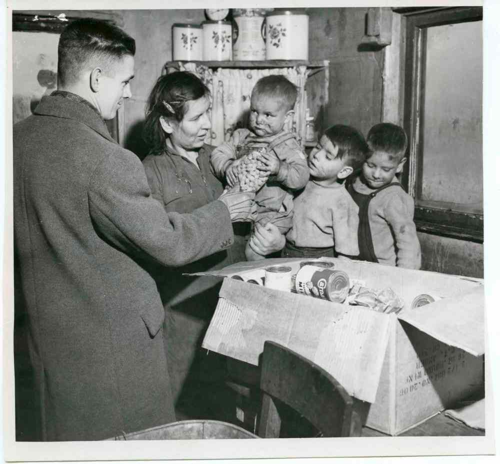 University of Manitoba Archives & Special Collections,  Winnipeg Tribune fonds
December 24, 1951:  After seeing a Tribune story describing the squalor of the Metis shack settlement in the southwest part of the city, an MTS group used $10 of an office fund to buy groceries for a needy family of the area. Shown presenting the groceries to Mrs. Archie Cardinal and three of her eight children is Joe Peters, head of the plants records department.