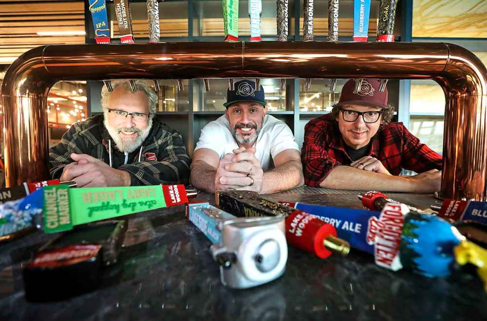 From left: Taras Manzie, president Lake of the Woods Brewing Company, Bobby Mottola, Academy Hospitality and Rob Dokuchie, owner and marketing/brand manager, Lake of the Woods Brewing Company, pose for a photo as the taps are being installed during the final preparations at Hargrave St. Market and food hall at True North Square Square Monday.  (Ruth Bonneville / Winnipeg Free Press)