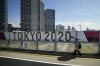 A woman walks on a bridge past a Tokyo 2020 banner ahead of the 2020 Summer Olympics, Saturday, July 17, 2021, in Tokyo. Tokyo is under a fourth state of emergency, which began Monday and requires restaurants and bars to close early and not serve alcohol through the games, which start July 23. (AP Photo/Jae C. Hong)