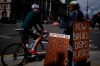 An environmental protester chats to a cyclist as he stands with placards and plastic bottles near the Houses of Parliament in London, Monday, Aug. 9, 2021. Earth's climate is getting so hot that temperatures in about a decade will probably blow past a level of warming that world leaders have sought to prevent, according to a report released Monday that the United Nations called a 