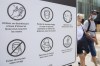 People wear face masks as they walk by a sign advising of COVID-19 prevention measures in Montreal on July 31, 2021. Canadians who refuse to wear a mask for non-medical reasons may be barred from casting ballots in person on Sept. 20. Chief electoral officer Stephane Perrault says in places where local public health rules require masking, Elections Canada will enforce those rules at polling locations. He&nbsp;encourages people who refuse to wear a mask to vote by mail instead. THE CANADIAN PRESS/Graham Hughes