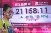 A woman wearing a face mask walks past a bank's electronic board showing the Hong Kong share index in Hong Kong, Tuesday, May 31, 2022. Asian shares were mixed Tuesday after reports showed China's manufacturing slowdown is moderating as anti-virus curbs on businesses in Shanghai and Beijing ease. (AP Photo/Kin Cheung)