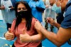 Doctor Anil Mehta, surrounded by his team of doctors, administers a dose of the Pfizer vaccine to Geeta Waddon to mark the 10,000th jab in his small practice in London, Sunday, Feb. 28, 2021. (AP Photo/Frank Augstein)