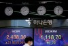 A currency trader walks near the screens showing the Korea Composite Stock Price Index (KOSPI), left, and the foreign exchange rate between U.S. dollar and South Korean won at the foreign exchange dealing room in Seoul, South Korea, Monday, Nov. 9, 2020. (AP Photo/Lee Jin-man)