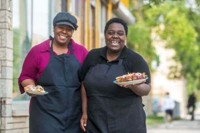 Deidré Coleman (left) and Patrice Gilman are taking part in this month's Black History Manitoba block party, dishing up Caribbean food from their West End restaurant. (Mikaela MacKenzie / Winnipeg Free Press)