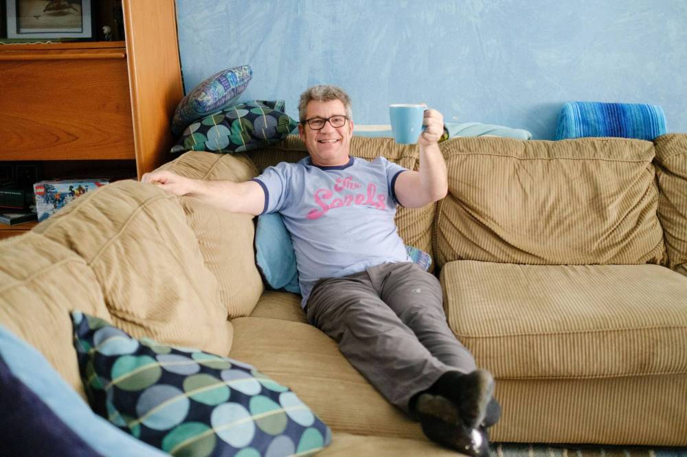Russell Morden lounges on the couch with his coffee cup, much like he did when he and his family contracted COVID-19. (Mike Sudoma / Winnipeg Free Press)
