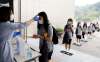 Students wearing face masks to help protect against the spread of the coronavirus stand in a line to have their body temperatures checked before entering their classrooms at a middle school in Chungju, South Korea last month. (In Jin-hyun / Newsis files)