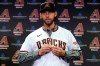 FILE - In this Dec. 17, 2019, file photo, newly acquired Arizona Diamondbacks pitcher Madison Bumgarner puts on a jersey after being introduced during a team availability in Phoenix. The Diamondbacks added a handful of veteran free agents during the offseason, including Bumgarner, outfielder Kole Calhoun, catcher Stephen Vogt and reliever Héctor Rondón. The left-handed Bumgarner — a four-time All-Star and 2014 World Series MVP — was the marquee signing, joining the rotation on an $85 million, five-year deal. (AP Photo/Matt York, File)