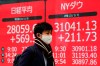 A man wearing a protective mask to help curb the spread of the coronavirus walks past an electronic stock board showing Japan's Nikkei 225 and New York Dow indexes at a securities firm Friday, Jan. 8, 2021 in Tokyo. Japan’s state of emergency to combat surging coronavirus cases, which kicked in Friday, did little to dampen market optimism. The benchmark Nikkei 225 surged 2.4% to close at 28,139.03, its highest finish in more than 30 years. (AP Photo/Eugene Hoshiko)