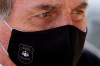 FILE - In this May 26, 2020 file photo, Brazil's President Jair Bolsonaro, wearing a face mask with a logo of the Federal Police, leaves his official residence of Alvorada Palace in Brasilia, Brazil. Bolsonaro won the presidency in 2018 with a campaign that emphasized law and order, and said police should be able to kill criminals with almost no legal constraints in order to curb homicides. (AP Photo/Eraldo Peres, FIle)