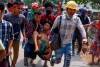 Anti-coup protesters carry an injured man following clashes with security in Yangon, Myanmar Sunday, March 14, 2021. The civilian leader of Myanmar's government in hiding vowed to continue supporting a 