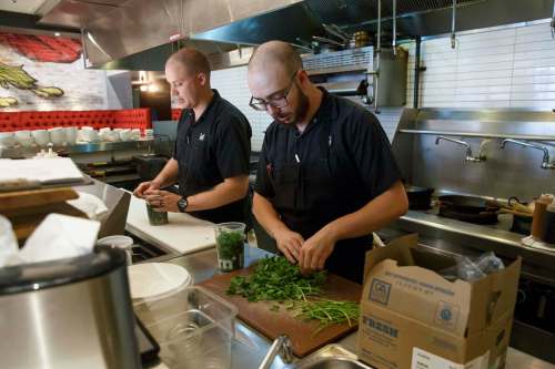 Opening line cook Ian Shapira (right) prepares cilantro for the day while executive chef Jesse Friesen (left) starts organizing for the opening in an hour.