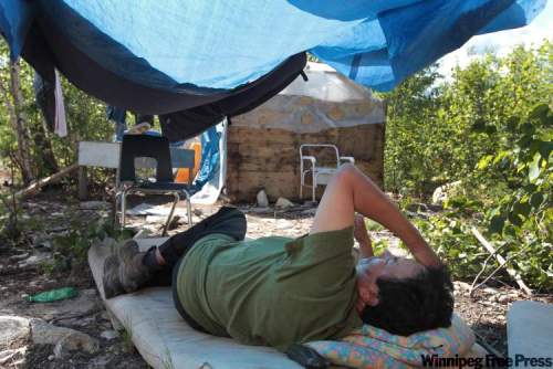 JOE.BRYKSA@FREEPRESS.MB.CA
Bernard Flett lies under a tarp to get out of the hot sun. After living without running water, he waits as crews renovate his St. Theresa Point home and install plumbing.