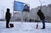 Workers clear the snow next to a billboard with a portrait of a Russian soldier awarded for action in Ukraine and the words 