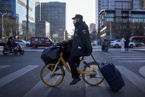 A security guard wearing a face mask and using a bike-sharing service carries his belonging rides across a street in Beijing, Monday, Jan. 9, 2023. China's healthcare authorities declined to include Pfizer's COVID-treatment drug in a national reimbursement list that would've allowed patients to get it at a cheaper price throughout the country, saying it was too expensive. (AP Photo/Andy Wong)