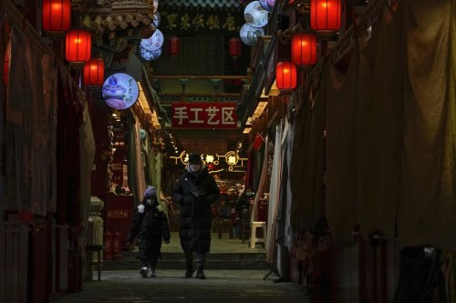 A man and a child wearing face masks walk by shuttered stores on Jan. 3, 2023, which would be selling souvenirs in Qianmen, a popular tourist spot in Beijing. China’s business and consumer activity might revive as early as the first quarter of this year, but before that happens, entrepreneurs and families face a painful squeeze from a surge in cases that has left employers without enough healthy workers and kept wary customers away from shopping malls, restaurants, hair salons and gyms. (AP Photo/Andy Wong)