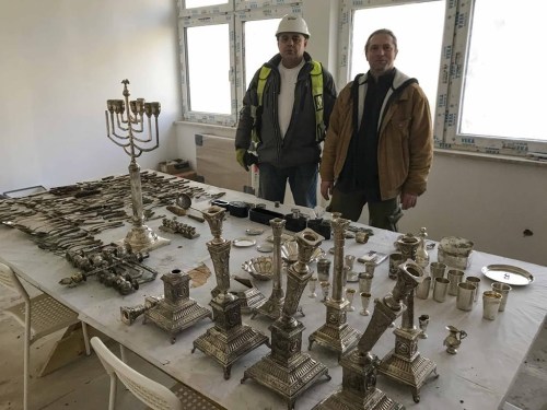 Krzysztof Hejmanowski, left, building inspector of the Warbud construction company and archaeologist Bartlomiej Gwozdz, right, pose for a photograph with objects that were most probably hidden by their Jewish owners during World War II, in Lodz, Poland, Wednesday, Jan. 11, 2023. Lodz city authorities were showing to The Associated Press and commenting about some 400 items - including silver-plated menorahs, hanukkiahs, tableware and daily use items, that were uncovered there last month during house and yard renovation works. (AP Photo/Rafal Niedzielski)