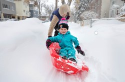 Five-year-old Thea Smoliak laughs as she holds on tight while her sled turns on its side due to snow drifts as her mom Shauna Smoliak pulls her home from school. (Ruth Bonneville / Winnipeg Free Press)