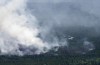 A helicopter carrying a water basket flies past a smoke plume near Lebel-sur-Quévillon, Que., Wednesday, July 5, 2023. THE CANADIAN PRESS/Adrian Wyld