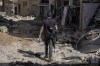 A Palestinian militant walks past an area damaged after an Israeli military raid in Jenin refugee camp in the West Bank, Friday, Nov. 10, 2023. (AP Photo/Majdi Mohammed)