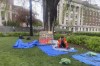 FILE - A graduate student in orange rolls up tents in front of a sign that says 