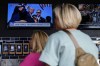 People watch news near the Fiserv Forum ahead of the 2024 Republican National Convention, Saturday, July 13, 2024, in Milwaukee. Former president Donald Trump was whisked off the stage at a rally in Butler, Pennsylvania after apparent gunshots rang through the crowd.(AP Photo/Matt Rourke)