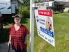 Supplied
                                Roseanne Milburn standing in front of a for sale sign at her home in Elie, Man. Her and her husband, Dan, are moving to Alberta in hopes she&rsquo;ll be fast-tracked for a double knee replacement, a procedure she&rsquo;s been waiting on for six years in Manitoba. Her knees cause her excruciating pain and she now relies on walking aids like canes, crutches and walkers. The stress from her condition has also led to permanent hair loss, forcing her to wear wigs and hats in public.