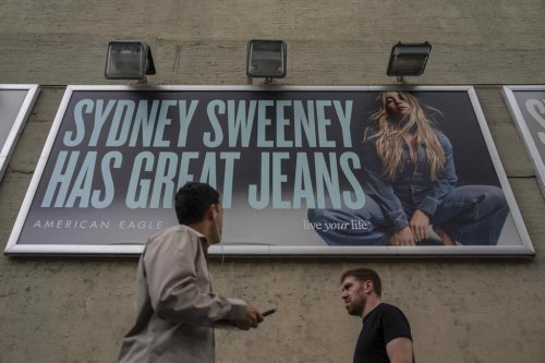 FILE - People walk past a campaign poster starring Sydney Sweeney which is displayed at the American Eagle Outfitters store, Friday, Aug. 1, 2025, in New York. (AP Photo/Yuki Iwamura, File)