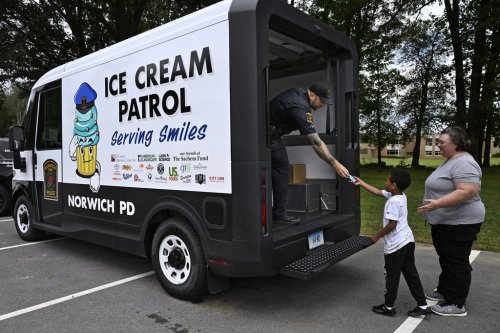 Norwich Police School Resource Officer Bob McKinney hands an ice cream to Alby Little as his mother Sylvia Little, right, looks on in Norwich, Conn., on Thursday, Aug. 21, 2025. (AP Photo/Jessica Hill)
