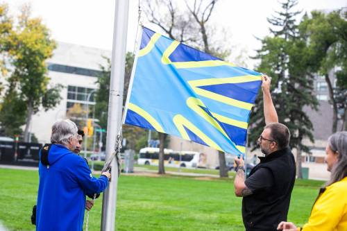 MIKAELA MACKENZIE / FREE PRESS
                                Manitoba Deaf Association board members Doug Momotiuk (left) and Kayle Miller raise the deaf flag in Memorial Park in front of the Legislative Building on Tuesday.