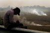 FILE - A person checks his mobile phone as farmers burn crop residue after harvest near Bundelkhand expressway in India, on Nov. 17, 2024. (AP Photo/Manish Swarup, File)